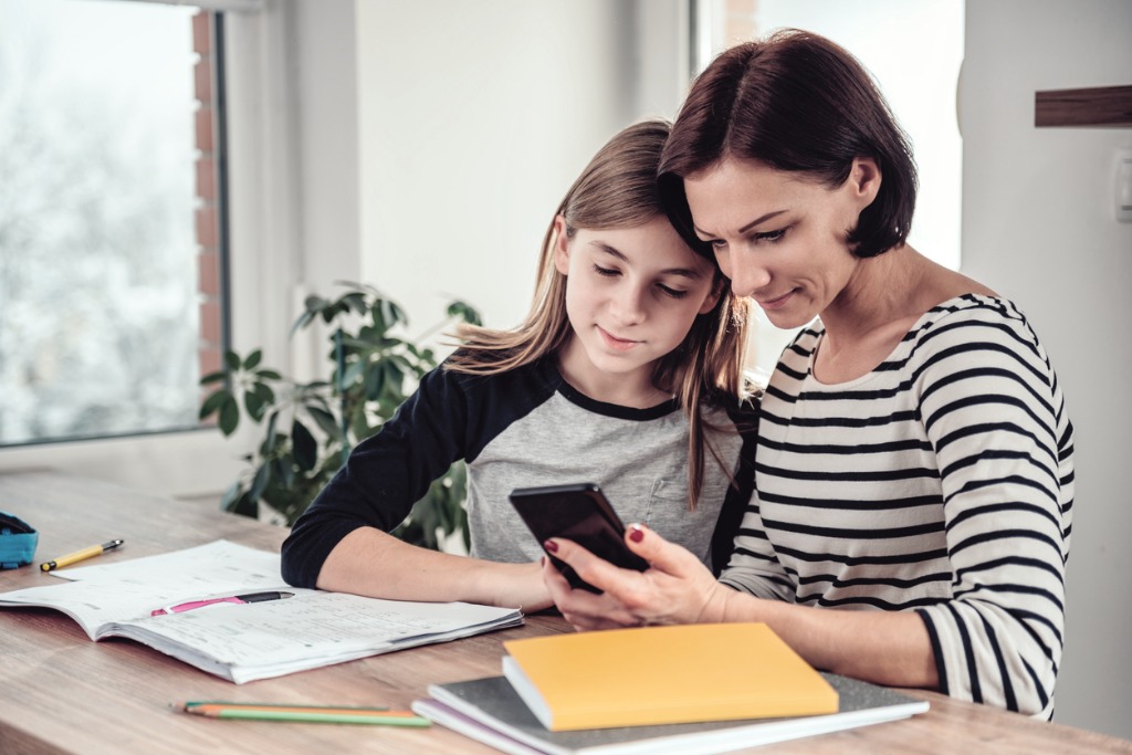 mother using smart phone and helping daughter with homework
