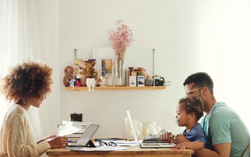 man and woman working on computers at table with toddler