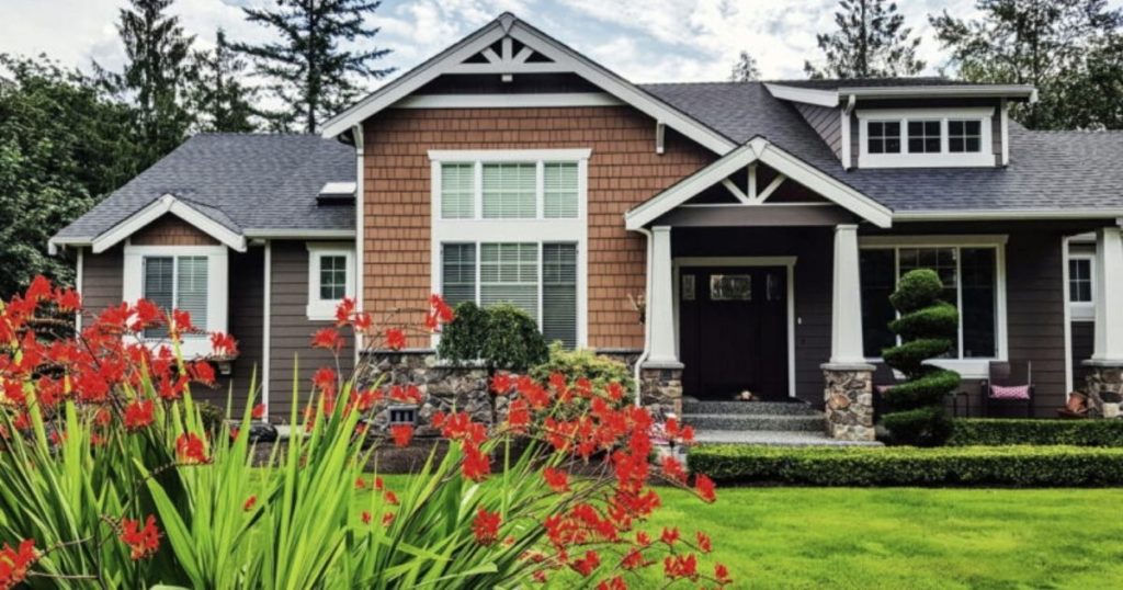 nice house with trees in back and red flowers in front