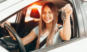 young woman holding car keys while sitting in drivers seat