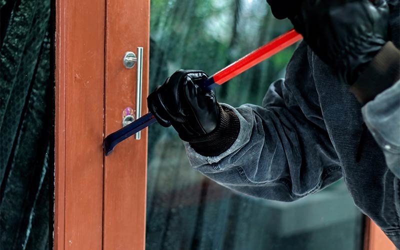gloved burglar using crow bar to break in to door on home