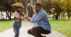 father puts on son's bike helmet