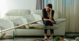 Sad female sitting on couch surrounded by home items after break in