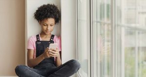 Young girl using cell phone by a window