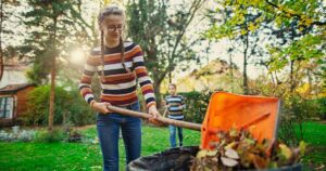 Young female scooping a pile of leaves into a trash can