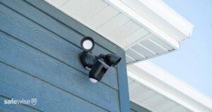 ring floodlight camera mounted to blue house near roofline