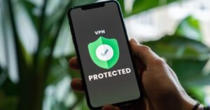 A man is holding an iPhone, the screen displays a green shield with the words 'VPN protected'