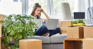 Young woman sitting on the sofa using laptop while moving in to new apartment