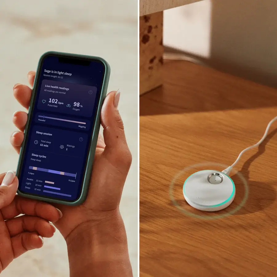 Parent holding the Owlet Dream app showing baby sleep and oxygen data next to the Owlet Dream Sock base station on a wooden nightstand.