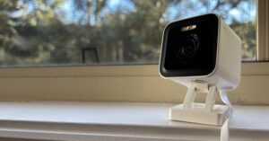 Wyze Cam v3 Pro sitting on a white windowsill against a window looking out onto trees