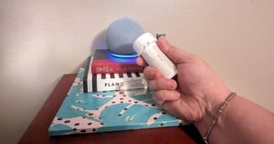 Amazon Echo dot speaker lit up on top of books with a hand holding prescription bottle nearby