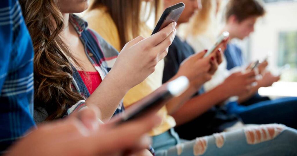 Close Up Of A Line Of High School Students Using Mobile Phones