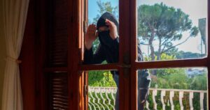 Burglar in balaclava peeks through the windows.