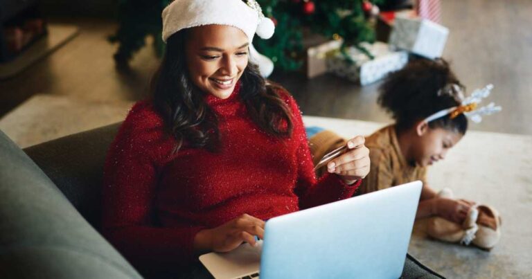 Shot of a young moom using a laptop and credit card with her daughter playing in the background during Christmas at home stock photo
