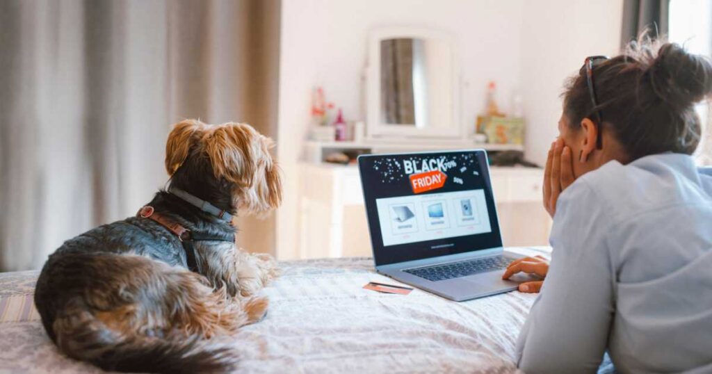 Woman is buying electronics online at Black Friday while relaxing at the bed with her dog.