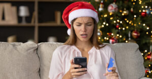 Worried concerned girl in Christmas Santa hat having problems with payment by credit card online for New Year purchases, looking at smartphone screen with puzzled face. Scam, fraud concept