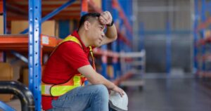 Tired, hot Asian male worker sitting resting in warehouse.