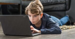 Young boy on floor looking intently at a laptop.
