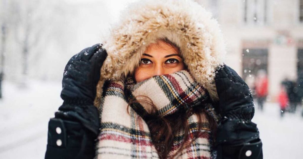 Woman bundled up in coat, scarf, hood outside in cold winter weather.