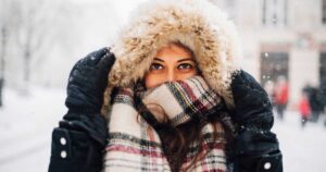 Woman bundled up in coat, scarf, hood outside in cold winter weather.