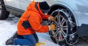 Man in orange parka putting snow chains on a tire.