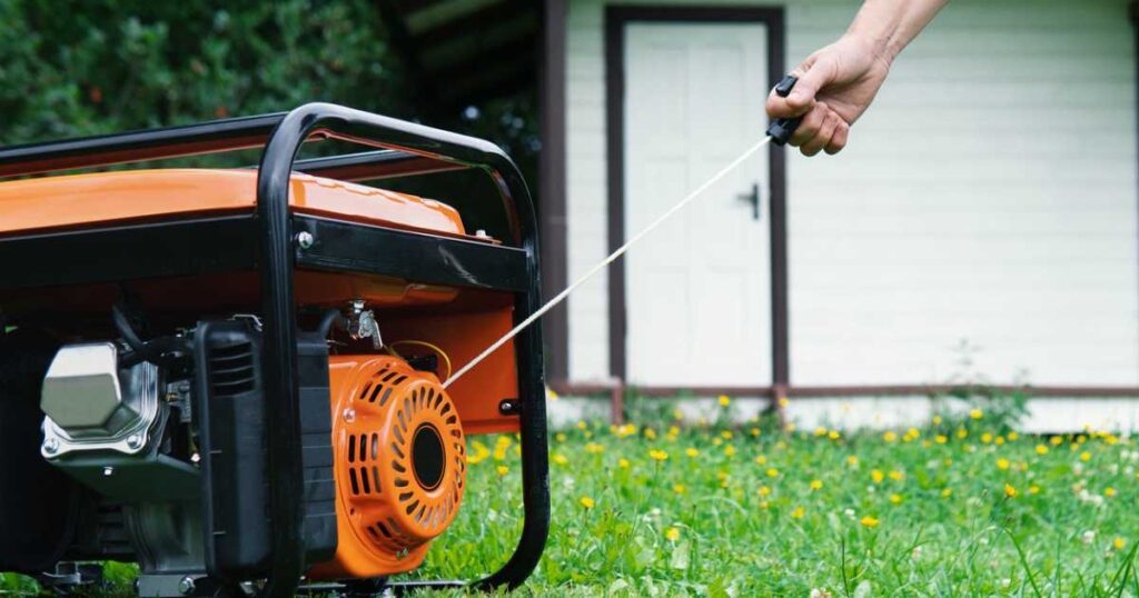 Hand starts a portable electric generator in front of a house in good weather.