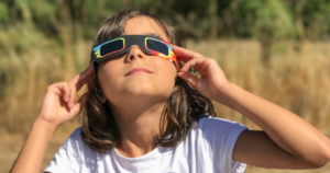 child watches eclipse with safety glasses