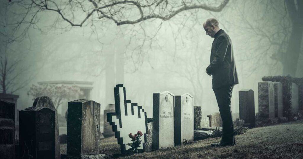 Man in graveyard by gravestone in the shape of a hand cursor
