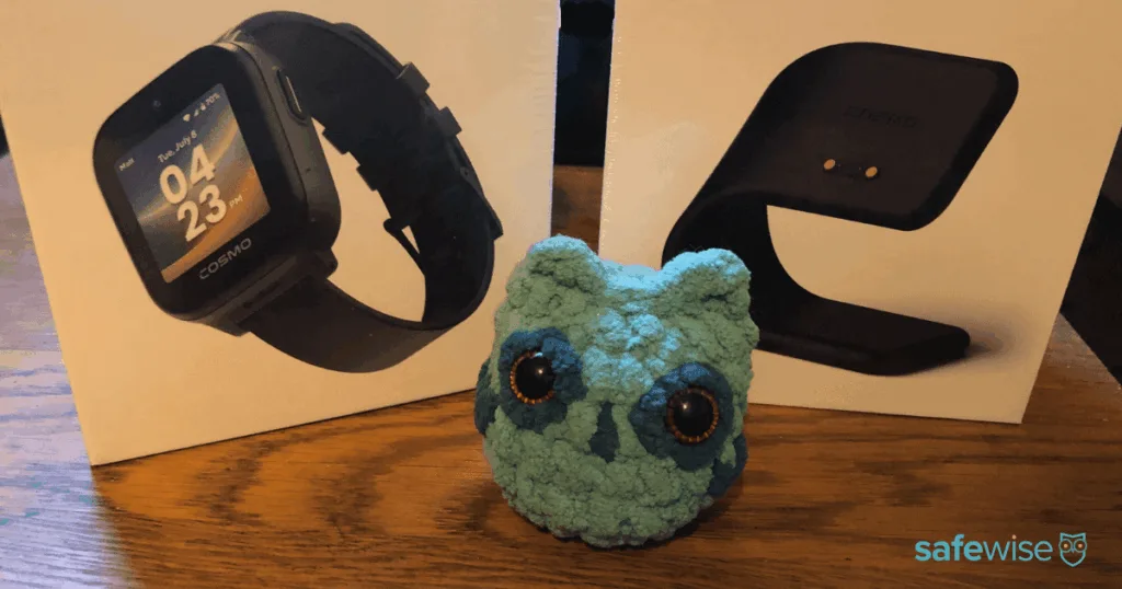 The SafeWise mascot in front of the COSMO JrTrack 5 watch and charging stand boxes.