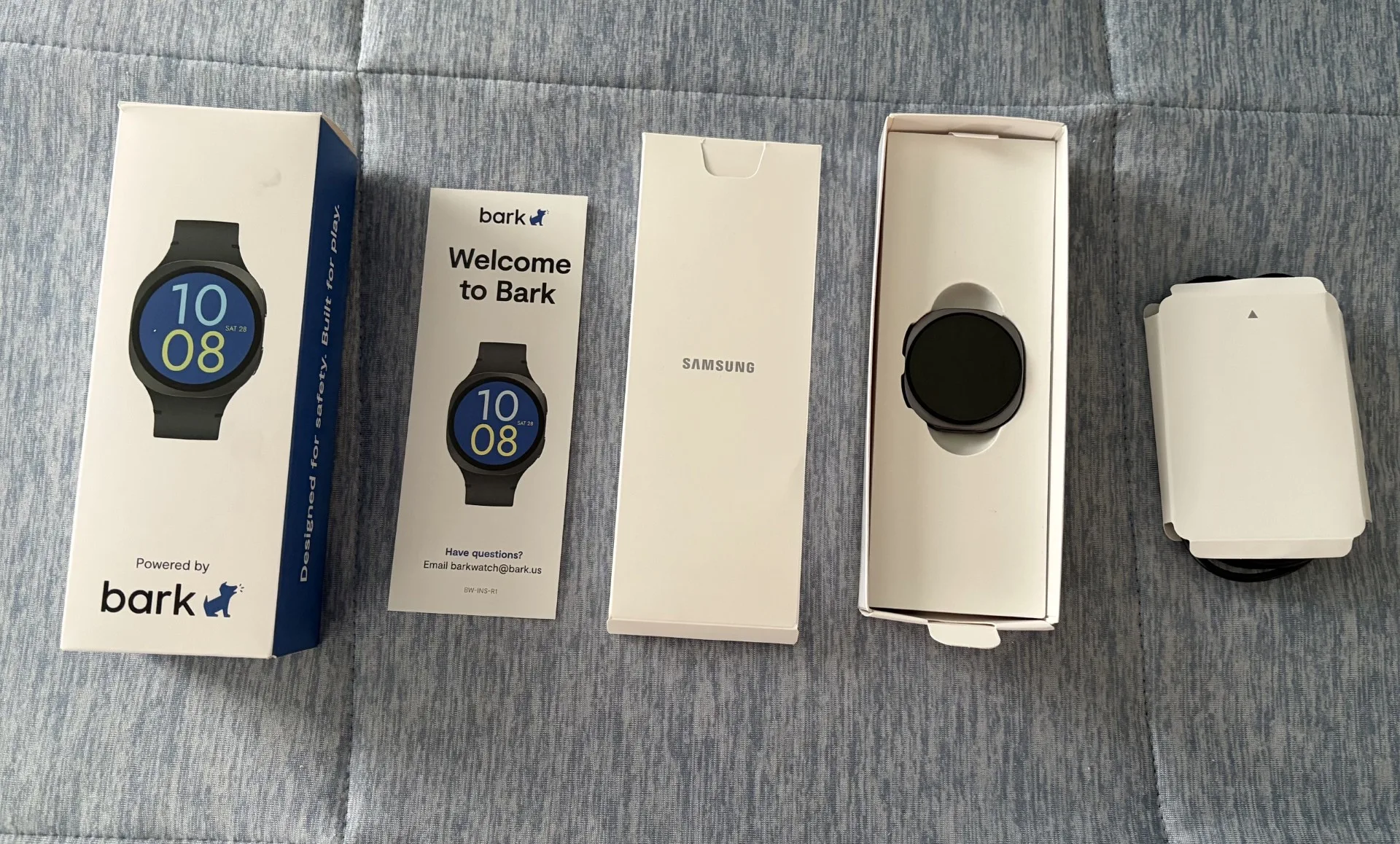 Collection of Bark smartwatch boxes and packaging components arranged on a gray fabric surface, including the main product box, welcome guide, Samsung box, and watch display boxes.