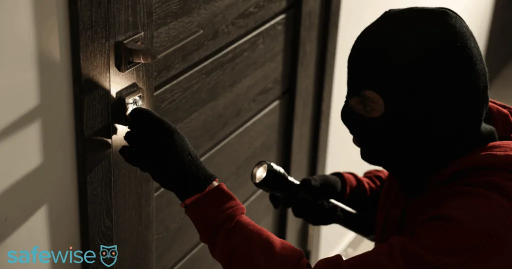 Burglar trying to break in while holding a flashlight
