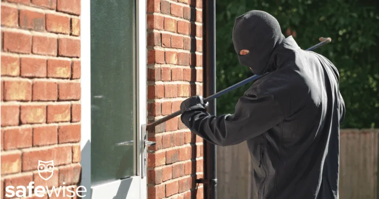 Burglar breaking into a home with a crowbar in daylight.