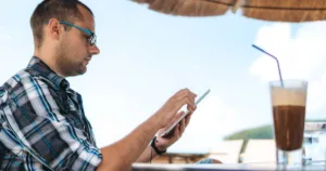 Young caucasian man checking in on his home on tablet and drinking ice coffee at seaside.