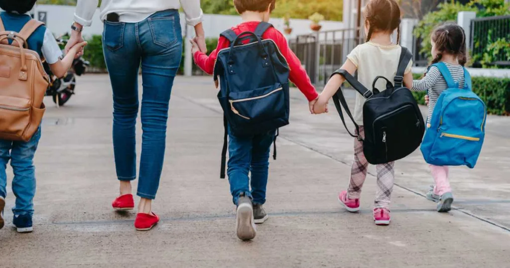Mother and kids holding hands going to school, with backpacks.