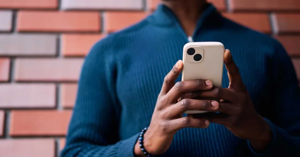 Close up of Black man holding smartphone, standing in front of a brick wall.