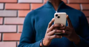 Close up of Black man holding smartphone, standing in front of a brick wall.