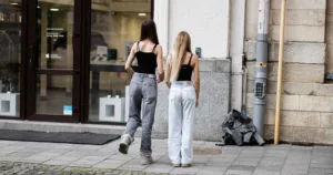 Two teen girls friends dancing for TikTok together in casual outfits outside a modern storefront