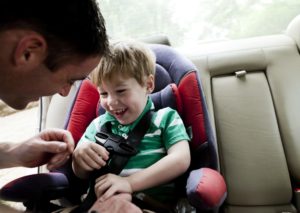 A father straps his son into a car seat.