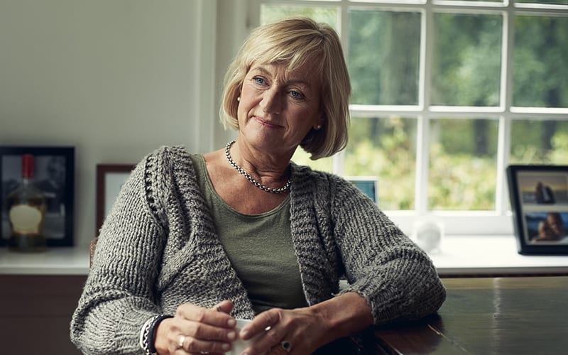 older woman in a sweater with a cup of coffee sitting in front of a window