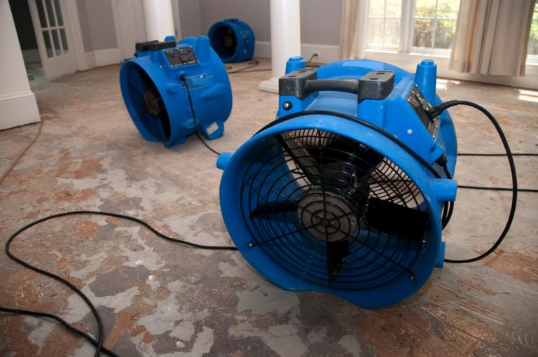 Large blue industrial fans in a flooded house on cement floor